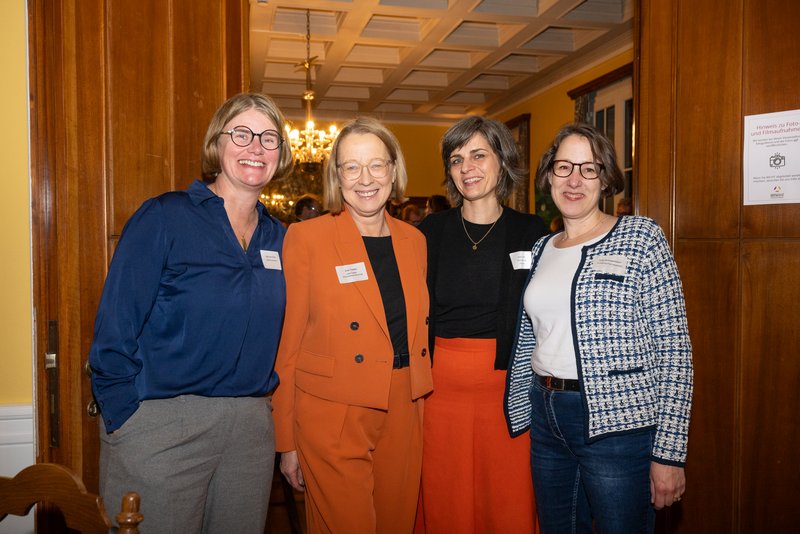 Das Bild zeigt vier Frauen, die lächelnd in einem Raum stehen. Sie scheinen an einer Veranstaltung teilzunehmen und strahlen eine freundliche, einladende Atmosphäre aus.