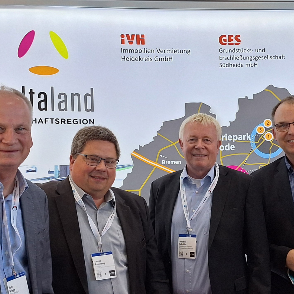 Messe REA 25 | Ⓒ Deltaland Das Bild zeigt vier Männer in Businesskleidung, die gemeinsam vor einem Messestand der Wirtschaftsregion „Deltaland“ stehen. Im Hintergrund sind Logos von regionalen Unternehmen und Institutionen wie der Kreissparkasse Walsrode sowie eine Karte mit den Standorten der Region zu sehen.