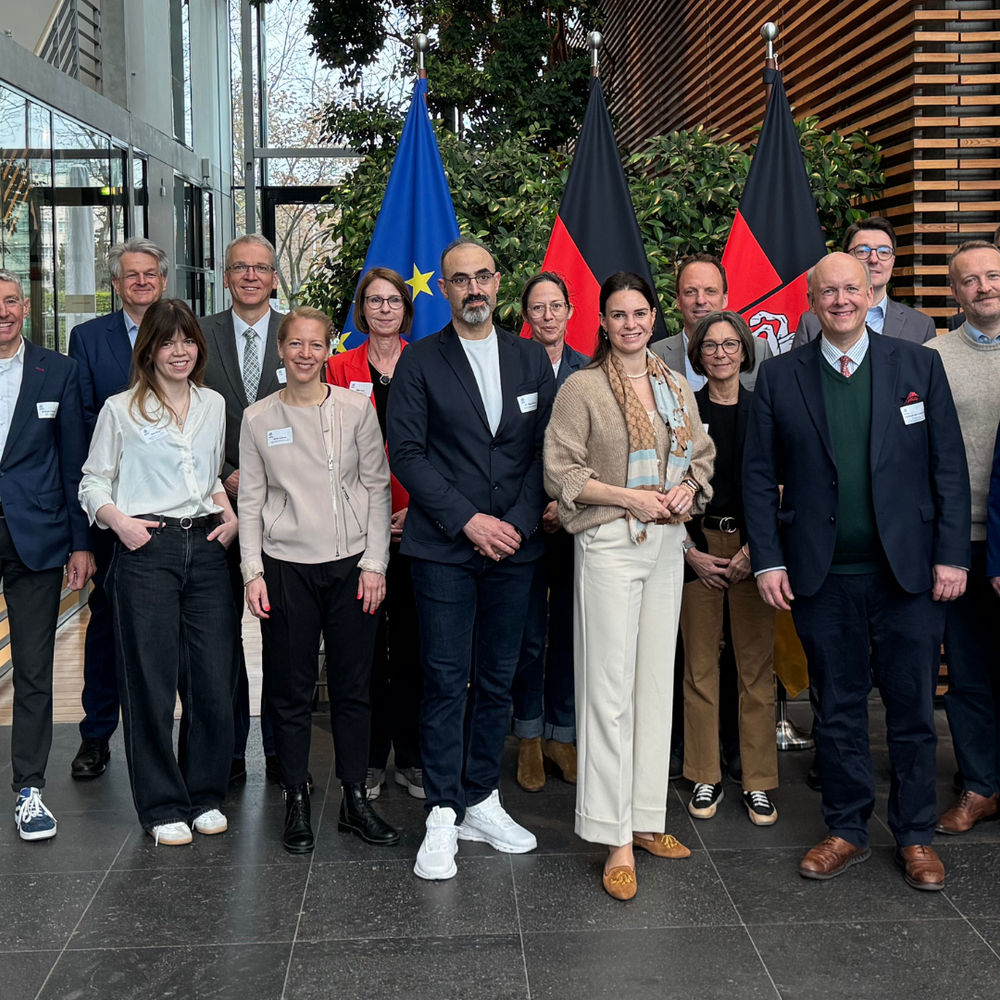 | Ⓒ H2.N.O.N-Regionalmanagement | Erstellt von: H2.N.O.N-Regionalmanagement Gruppenfoto der Teilnehmenden des dritten H2.N.O.N-Hauptstadtfrühstücks am 14. April 2026 in der Vertretung des Landes Niedersachsen beim Bund in Berlin. Vor EU-Fahne und Deutschlandfahne versammeln sich rund 20 Vertreterinnen und Vertreter aus Wirtschaft, Netzwerk und Politik zum gemeinsamen Austausch über den Markthochlauf der Wasserstoffwirtschaft.