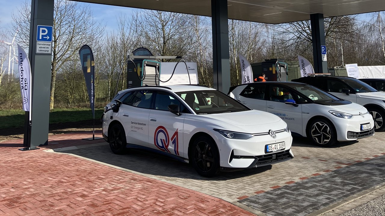 Das Bild zeigt mehrere Elektrofahrzeuge, die an einer modernen Ladestation geladen werden. Die Umgebung ist hell und freundlich, mit blauem Himmel und Bäumen im Hintergrund, was auf eine nachhaltige Mobilitätslösung hinweist.