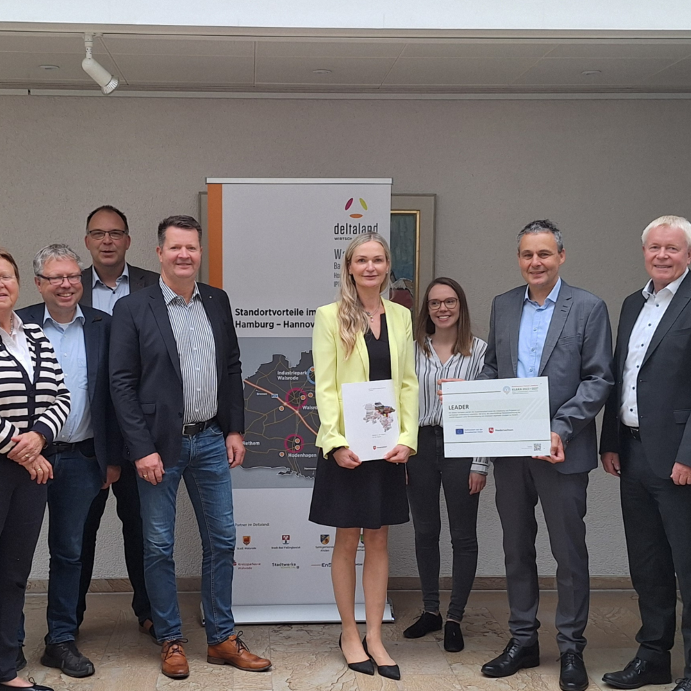 | Ⓒ Deltaland Auf dem Bild ist eine Gruppe von zehn Personen zu sehen, die in einem hellen Foyer gemeinsam posieren. In der Mitte halten zwei Personen einen Förderbescheid sowie eine Urkunde, was auf eine feierliche Übergabe hinweist. Personen auf dem Bild v.l.: Andre Popp, Industriepark Walsrode, Helma Spöring, Stadt Walsrode, Björn Gehrs, Samtgemeinde Schwarmstedt, Michael Krohn, Wirtschaftsförderung Deltaland, Carsten Niemann, Samtgemeinde Ahlden, Christiane Unruh, ARL Lüneburg, Laura Peters, Stadt Bad Fallingbostel, Cort-Brün Voige, ARL Lüneburg, Matthias Schröder, Kreissparkasse Walsrode, Björn Symank, Samtgemeinde Rethem (Aller).